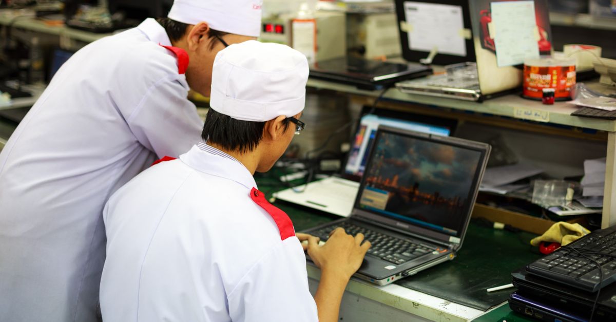 Two technicians in uniforms working on laptops in a laboratory setting. Focus on teamwork and technology.
