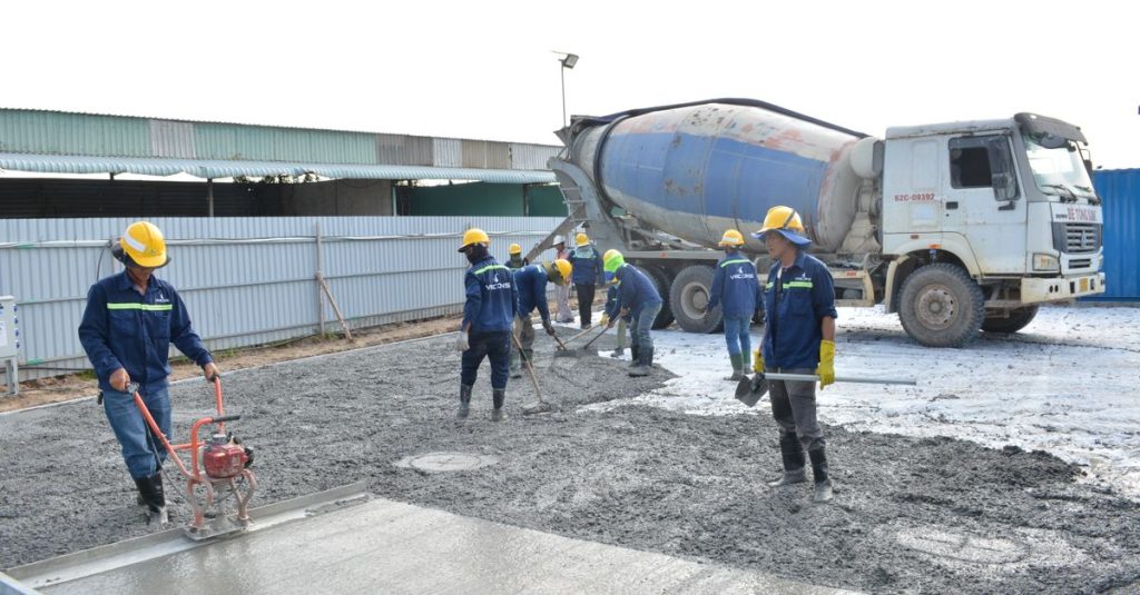 Công nhân làm việc với xe trộn bê tông tại công trường xây dựng.