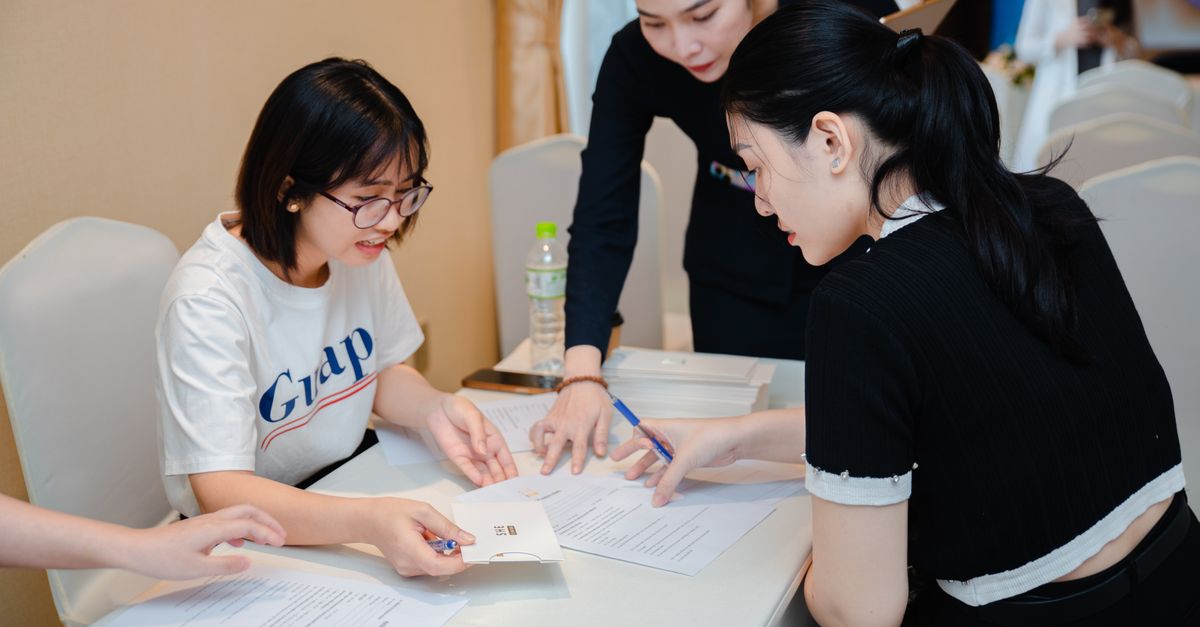 Three women collaborating in an indoor meeting, discussing documents at a table.