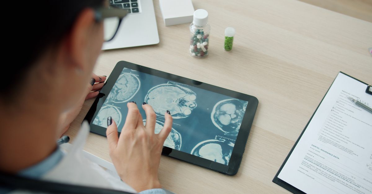 Doctor analyzing brain scans on a tablet in a clinical setting.