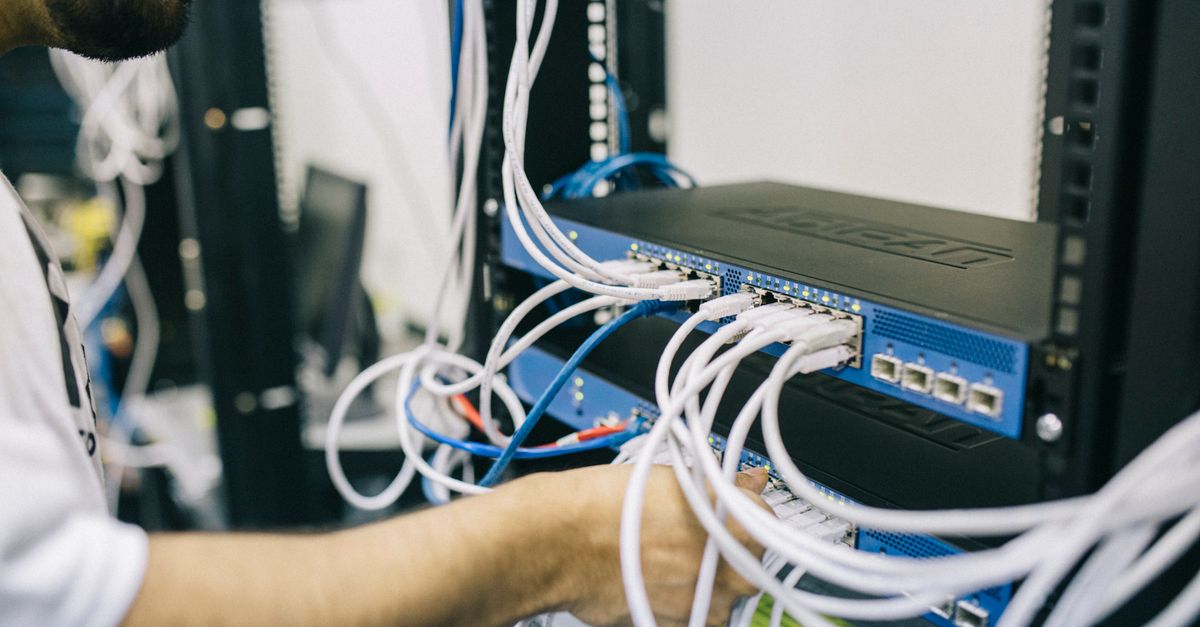 An IT professional configuring network cables in a server rack, focusing on Ethernet connections.