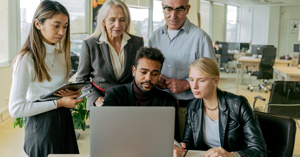A diverse group of professionals collaborating around a laptop in a modern office setting.