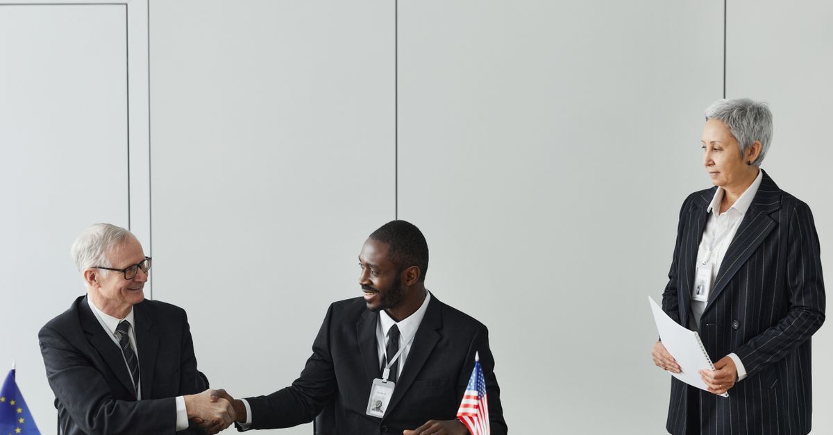 Multinational business meeting with agreement signing, featuring diverse professionals and flags.