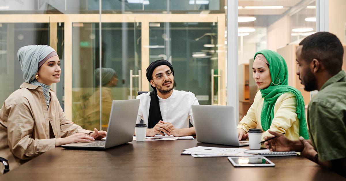 A diverse group discussing ideas in a modern office setting, using laptops and tablets.