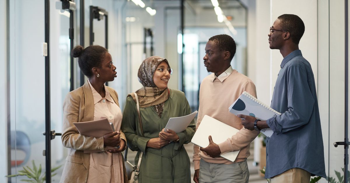A diverse group of colleagues engaged in conversation in a modern office hallway.