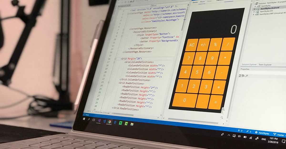 A laptop screen shows a coding application with a calculator design in a tech office setting.